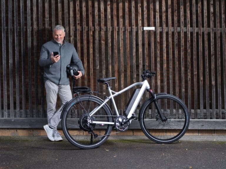 Mann vor Holzwand mit Smartphone und Helm in der Hand und einem AureusDrive Power45 E-Bike in Szene.